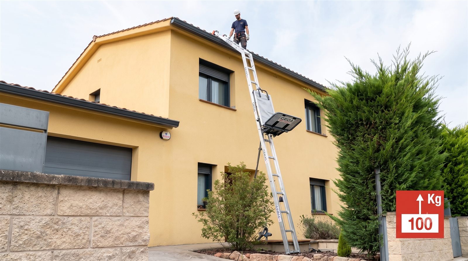 Elevador de escalera CAMAC 100 instalado en la fachada de una casa subiendo materiales al tejado, con capacidad de 100 kg